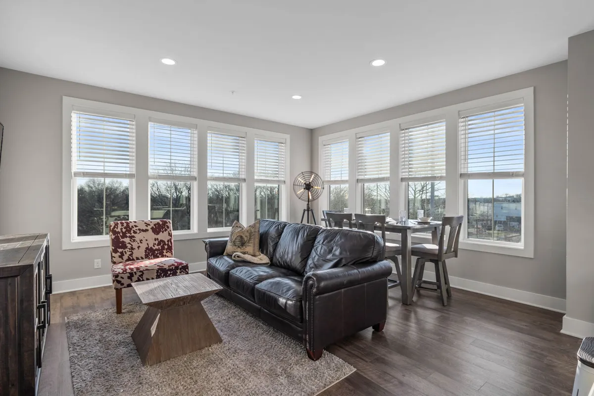 A cozy and stylish living room featuring a plush leather sofa, a colorful armchair, a dining table set for a group, and expansive large windows that flood the open-concept space with natural light. The room exudes comfort and is arranged to encourage both relaxation and social interaction.