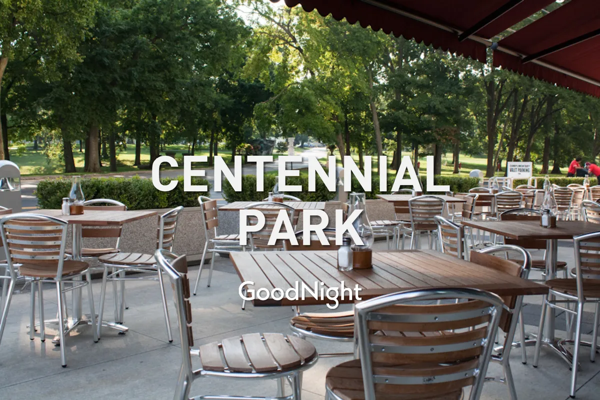 This exterior image shows tables with wooden tops and metal chairs set under a canopy, surrounded by lush greenery. The relaxed outdoor dining scene hints at the vibrant culinary culture and opportunities for couples to enjoy meals or drinks together, possibly at one of the neighborhood’s acclaimed restaurants.