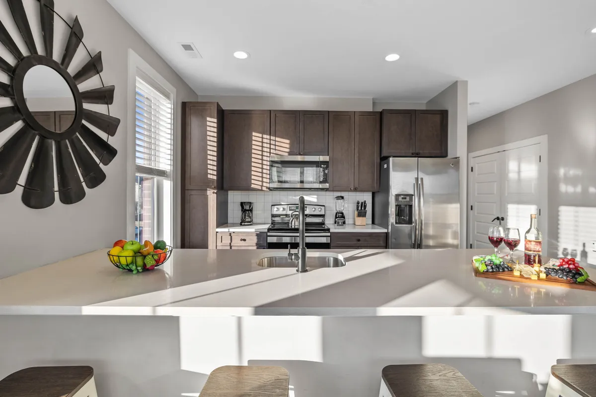 The photo centers on a kitchen island countertop adorned with a fruit bowl and wine glasses, surrounded by modern appliances. The scene feels vibrant and social, evoking an atmosphere where culinary creativity and casual gatherings blend seamlessly.