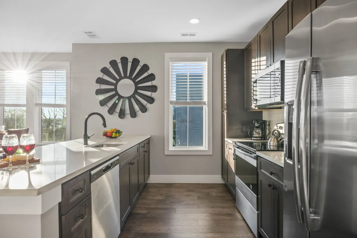This image showcases a modern kitchen with sleek cabinetry, a large window bringing in natural light, a decorative wall mirror, and a central kitchen island. The space is bright, open, and clearly set up for both cooking and entertaining, with details that suggest a welcoming and lively environment.