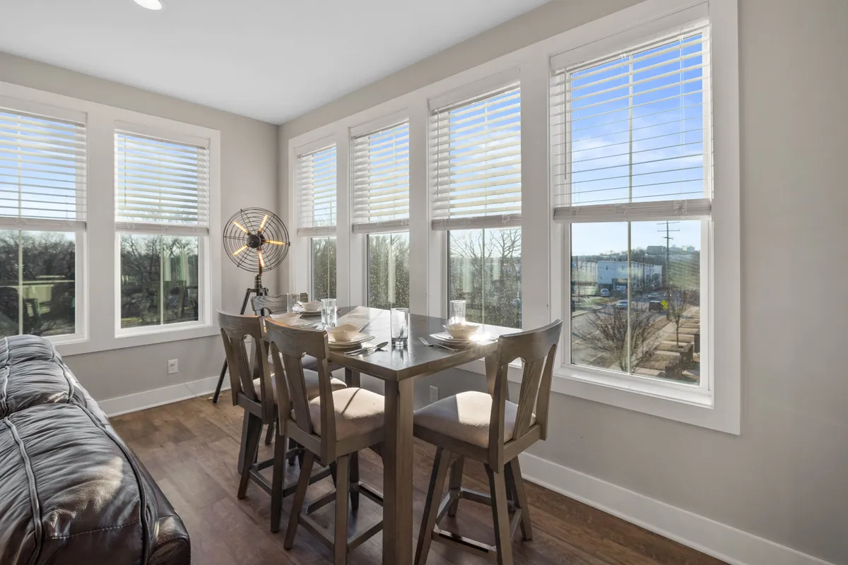This image displays a well-lit dining area featuring a sturdy dining table, windows allowing daylight to stream in, and a ceiling fan overhead. The ambience is relaxed, supporting both casual dining and more formal meal occasions.