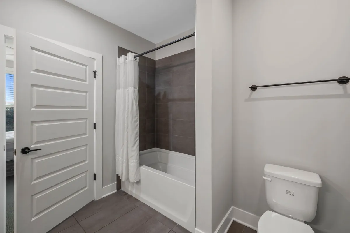 A clean and inviting bathroom with a bathtub, shower curtain, and toilet. The space is functional yet comfortable, suitable for guests needing easy access to a full bath.