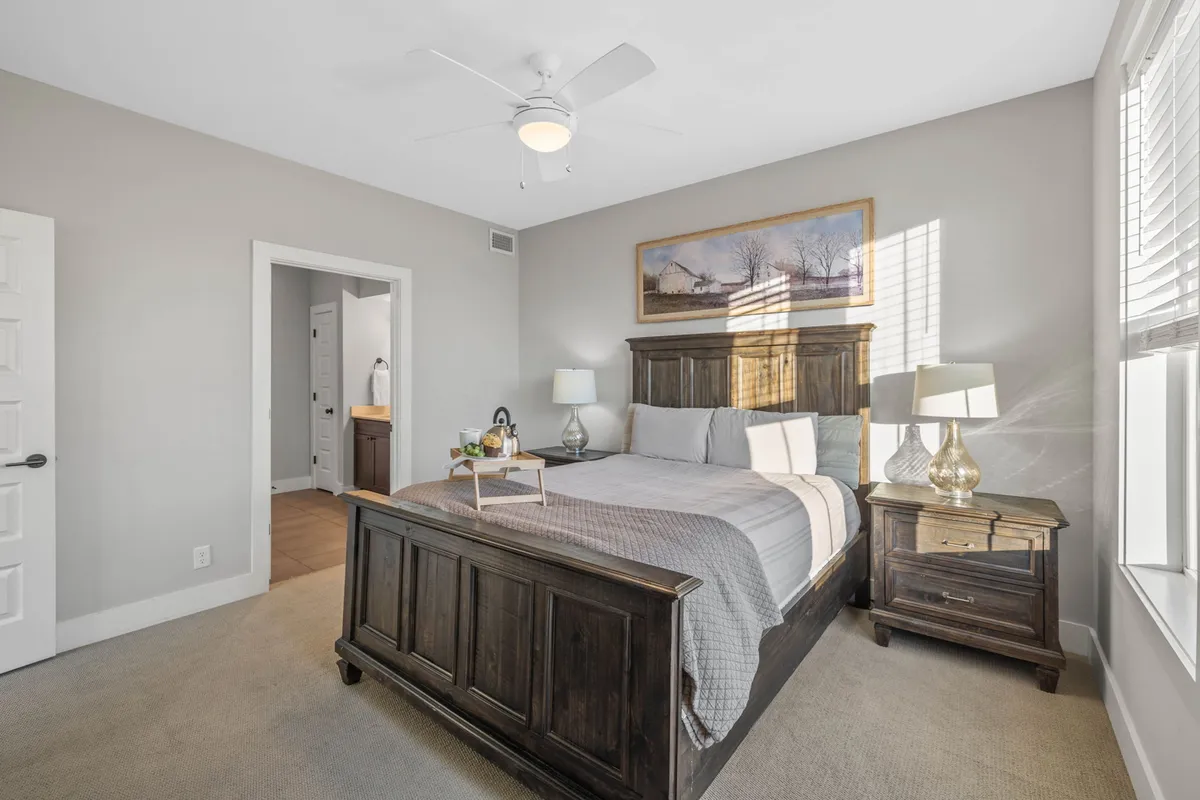 A cozy bedroom with a Queen bed, nightstands, soft lighting from a lamp, and stylish artwork. Natural light filters in, creating a peaceful setting for relaxation or reading.